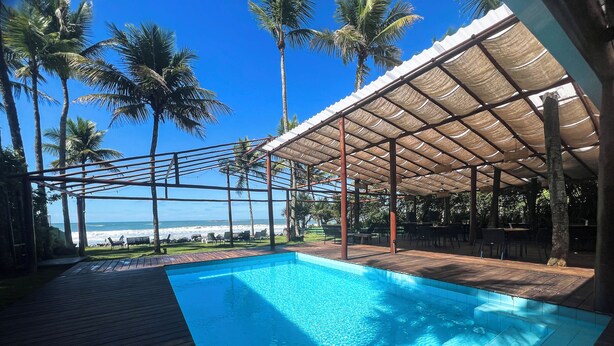 Un espace piscine avec vue sur la plage, entouré de palmiers et doté de coins salon abrités.