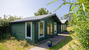 A small, green wooden cabin with a sloped roof, a porch, and a potted plant in front. - Clover at Gorslwyd - Sound Retreat (Cardigan)