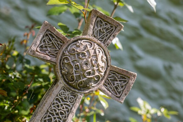 A stone cross with intricate carvings, set against a blurred natural background. - Clover at Gorslwyd - Sound Retreat (Cardigan)