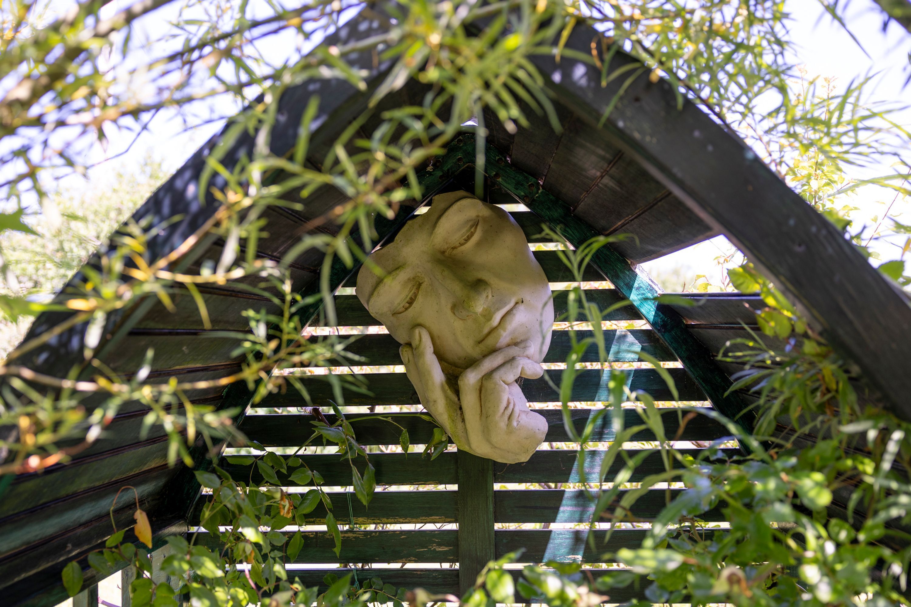 Una escultura de una mano con rostro, parcialmente cubierta por follaje.