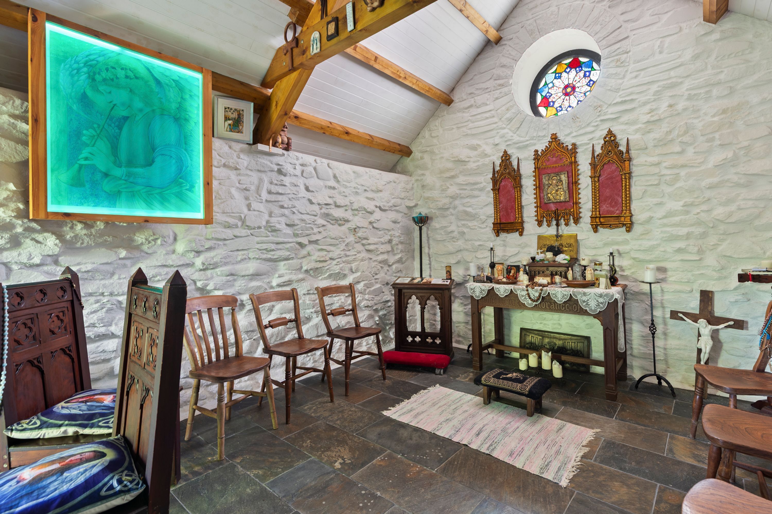 Ein Raum mit Steinsälen, Holzbalken, einem hölzernen Altar und einem Glasfenster mit Blei-Scheiben.