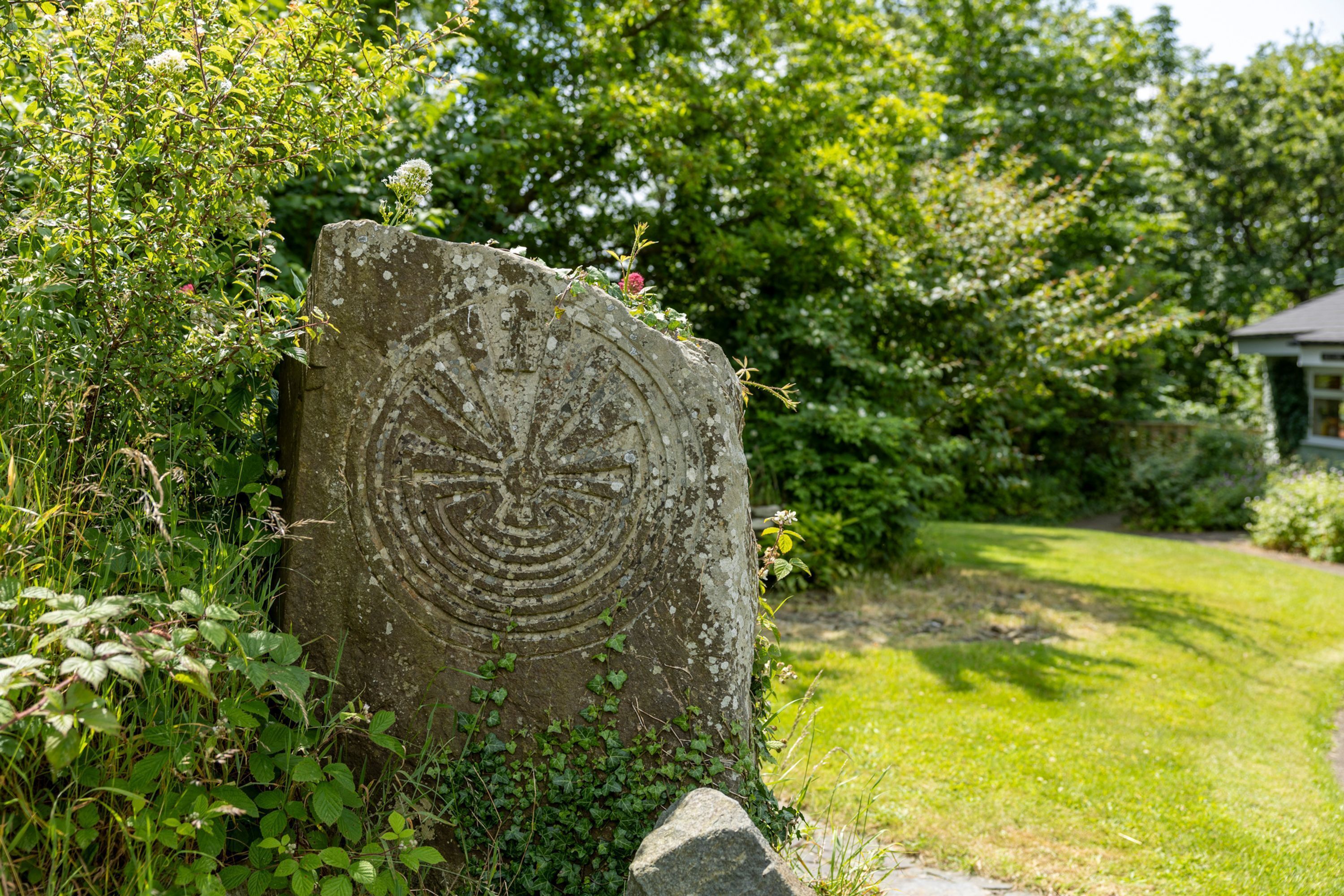 A large stone monument with a circular design, surrounded by lush greenery and trees.