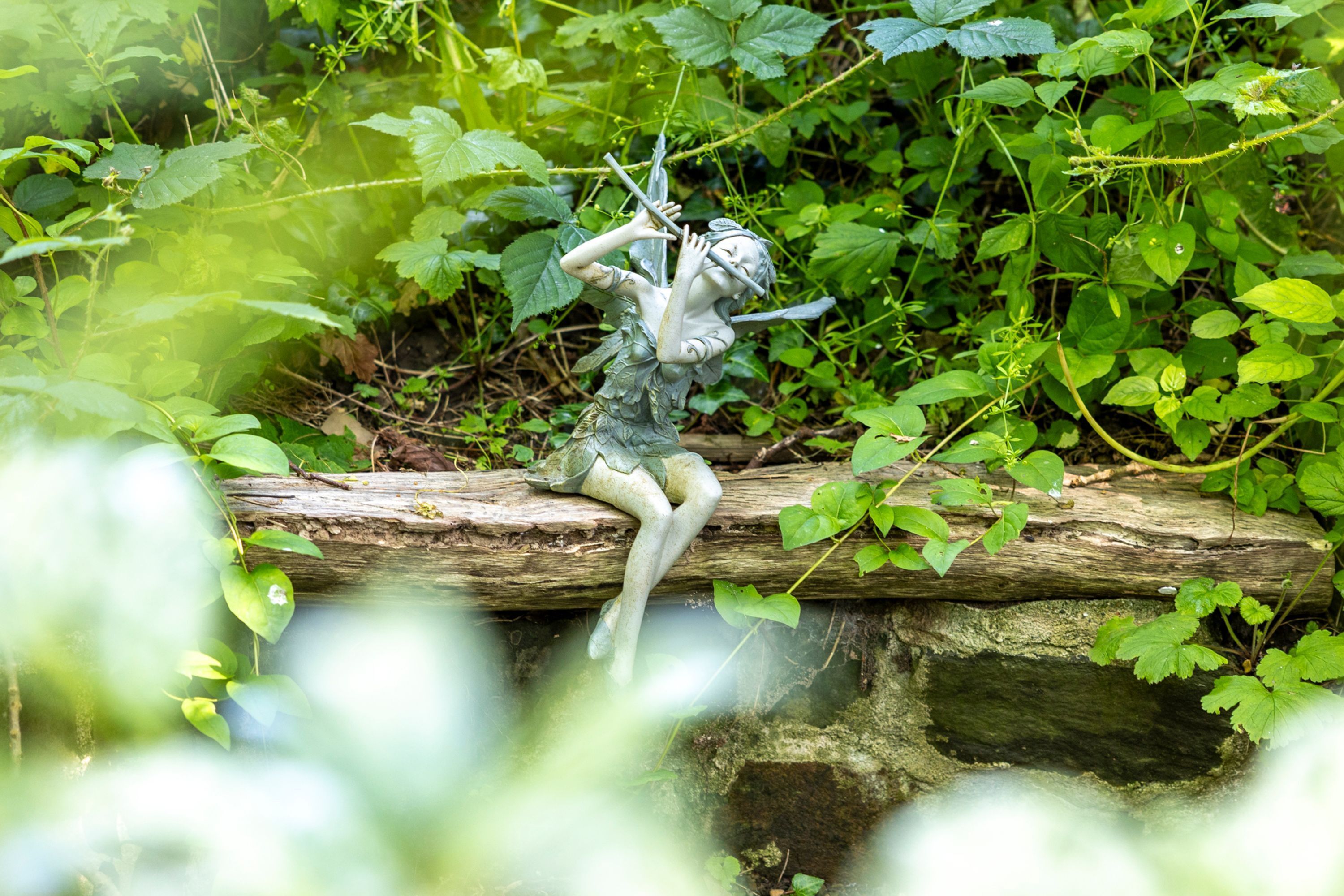 A statue of a figure with a bow and arrow, positioned on a log in a natural setting with greenery around.