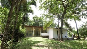 A modern house with a glass facade, surrounded by lush greenery and trees. - Airport Green Villa (Andiambalama)