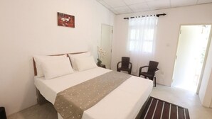 A hotel room with a bed, a chair, a small table, and a window with curtains. - Airport Green Villa (Andiambalama)
