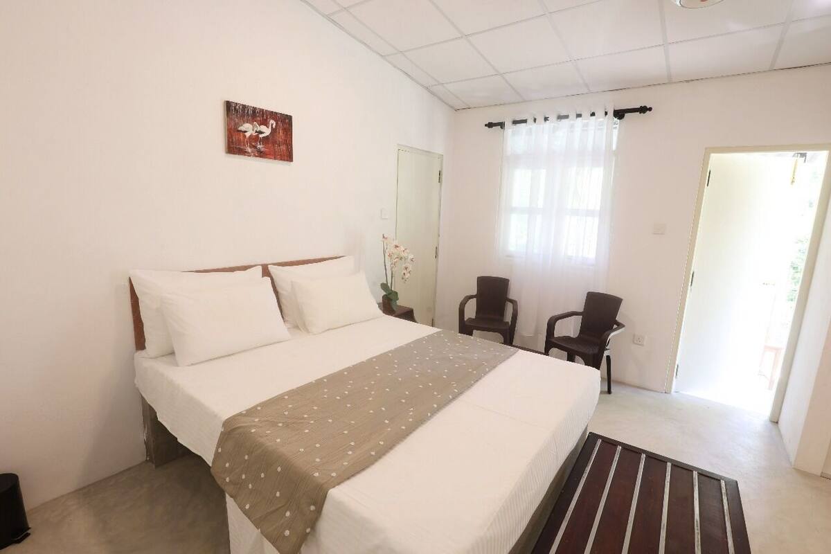 A hotel room with a bed, a chair, a small table, and a window with curtains.