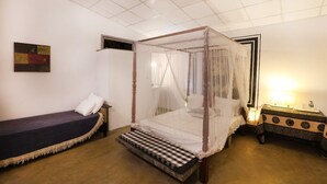 A room with a four-poster bed, a single bed, a bedside table with a lamp, and a wall-mounted painting. - Airport Green Villa (Andiambalama)