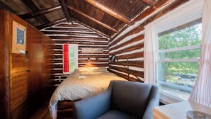 Una acogedora habitación de cabaña de madera con una cama, un sillón, una ventana con vistas al exterior y un letrero con un nombre en la pared.