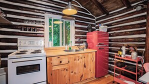 Cocina rústica de cabaña con interior de madera, estufa blanca, refrigerador rojo y encimera de madera.