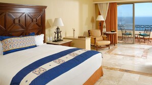 Habitación de hotel con una cama grande, una silla, una mesita y un balcón con vistas al mar.