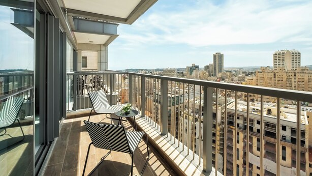 A balcony with a view of the cityscape, featuring a table with chairs and a potted plant.