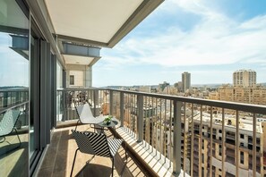 Un balcó amb vistes a la ciutat, amb una taula, cadires i una planta en test.
