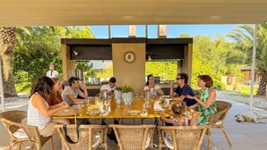 A group of people dining at an outdoor table with wicker chairs, surrounded by greenery. - Bartoli Estate - Bouganville Apartment (Mazzarino)