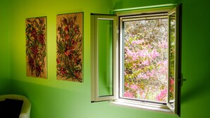 A room with green walls, two floral paintings, and a window with pink flowers outside. - Bartoli Estate - Bouganville Apartment (Mazzarino)