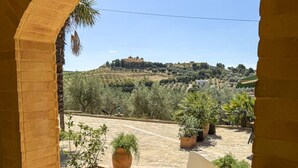 An outdoor patio area with a brick floor, potted plants, and a view of a hilly landscape. - Bartoli Estate - Bouganville Apartment (Mazzarino)