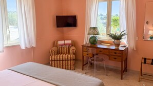 A bedroom with a bed, a desk, a chair, a TV, and a window with curtains.