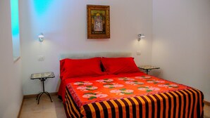 Une chambre à coucher avec un lit, des oreillers rouges, une couvre-lit à motifs floraux, deux tables de chevet et un cadre photo fixé au mur.