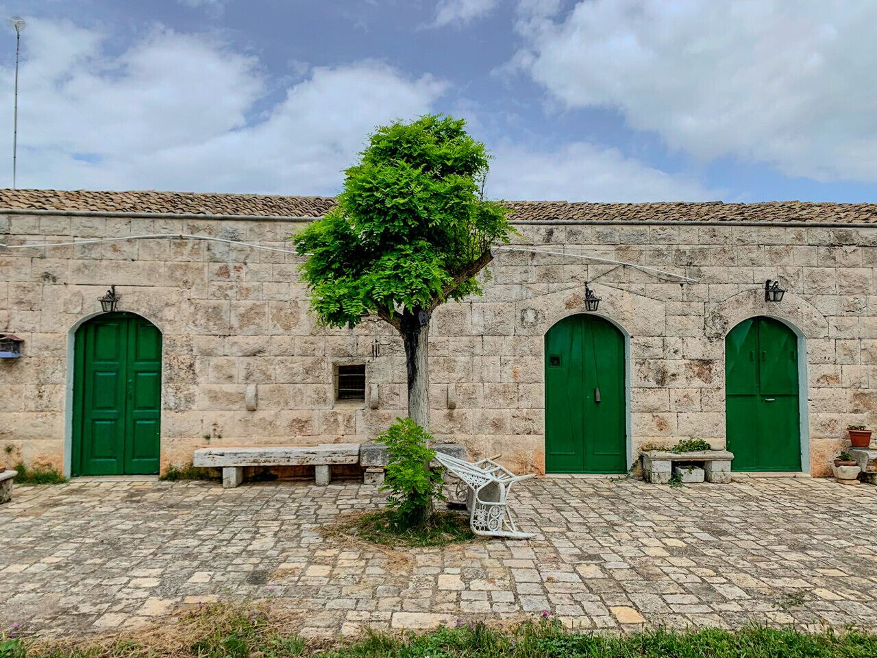 Ein Innenhof mit einem Steinhaus, der grüne Türen und einen Baum in der Mitte zeigt.