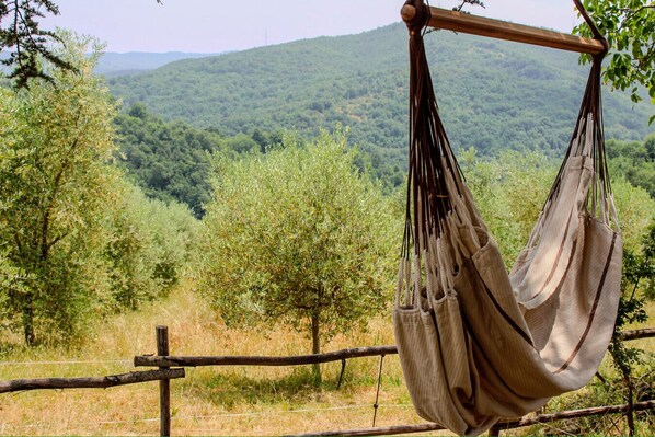 A hammock hanging on a wooden beam with a view of a forested mountain range.