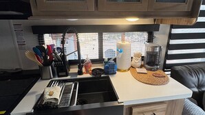 Et lille køkken med vask, komfur og bordplade. Der er skabe over vasken og en kaffemaskine på bordpladen.