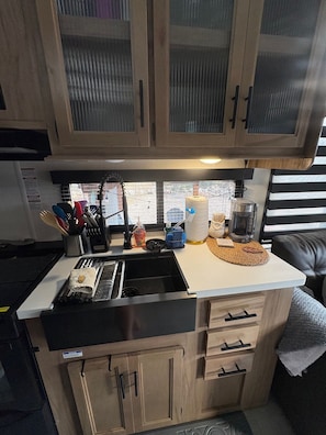 A compact kitchen with a sink, stove, and countertop. There are cabinets above the sink and a coffee maker on the countertop. - Enchanting Magical Modern Tiny Home; pet friendly (New Braunfels)