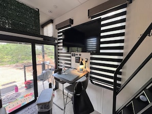 A compact room with a small table, a chair, a black bag, and a window with blinds. - Enchanting Magical Modern Tiny Home; pet friendly (New Braunfels)