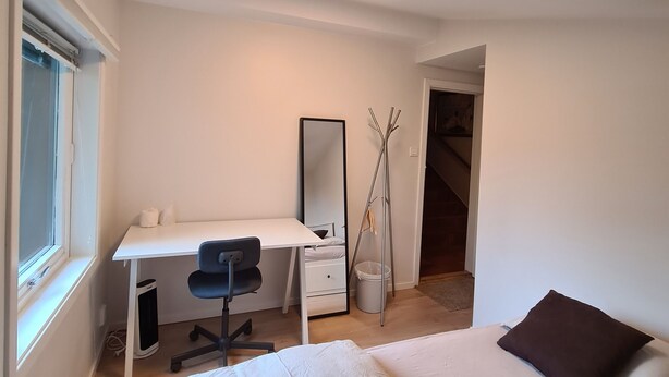 A bedroom with a bed, a desk, a chair, a mirror, and a window.