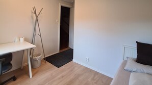 A modern bedroom with a bed, a desk, and a chair. There is a door leading to another room.