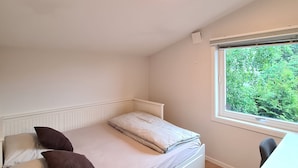 A bedroom with a bed, a desk, and a window with a view of greenery.