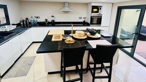 Cocina moderna con isla central, sillas negras y vista al exterior a través de una puerta de vidrio.