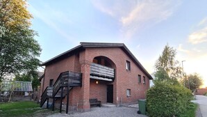 Un bâtiment en briques avec un escalier menant à un étage supérieur, un petit porche et une allée gravillonnée.
