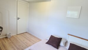 Une chambre à coucher avec un lit, une porte, un mur blanc et un luminaire au plafond.