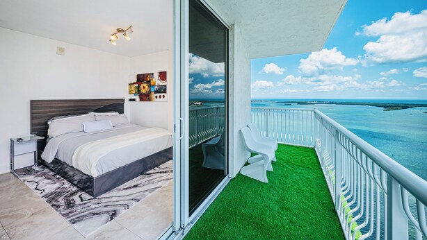 Un dormitorio con cama, mesita de noche, lámpara de pared y balcón con vistas al mar.