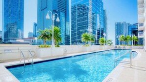 Una piscina con agua azul cristalina, rodeada de palmeras y edificios modernos al fondo.