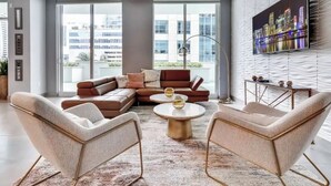 Una sala moderna con un sofá seccional, dos sillones, una mesa de centro y un televisor grande en la pared.