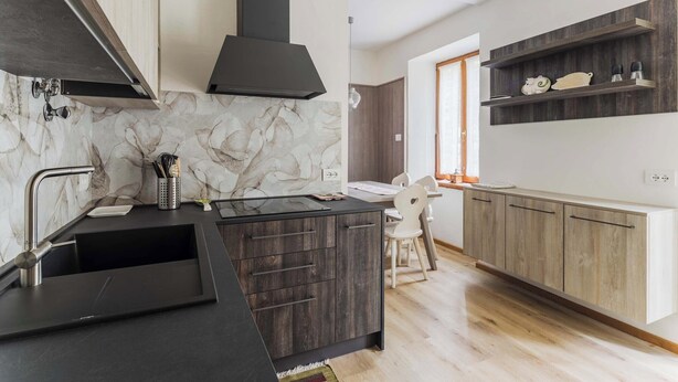 Una cocina moderna con salpicadero de mármol, armarios de madera oscura y una campana extractora negra.