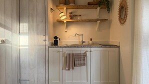 Una cocina con armarios blancos, una encimera, un fregadero y una toalla colgando. Hay estanterías con plantas y un espejo decorativo en la pared.