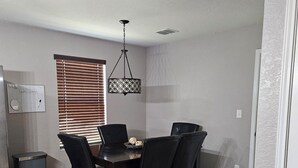 Un comedor con mesa y sillas de madera, una lámpara colgante con diseño y una ventana con persianas.