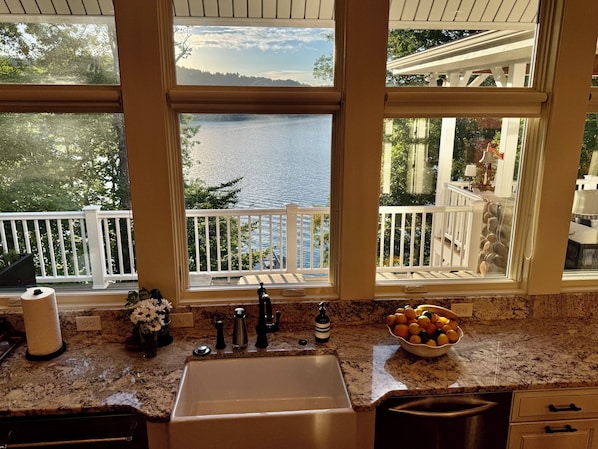 A kitchen with a large window, a sink, and a bowl of fruit on the counter.