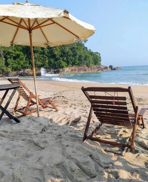 A beach with wooden lounge chairs and a large umbrella. - Shambhala Eco Suite by the Sea between Paraty and Ubatuba (Camburi Ubatuba)