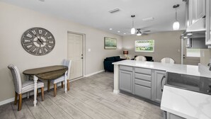 A modern kitchen with a wooden dining table, a large clock, and a view of the outdoors. - CRYSTAL BEACH GETAWAY-STEPS TO THE GULF (Crystal Beach)