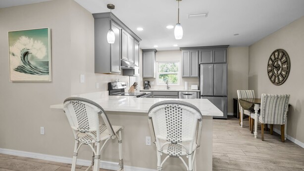 A modern kitchen with grey cabinets, a white island, and two wicker chairs. - CRYSTAL BEACH GETAWAY-STEPS TO THE GULF (Crystal Beach)