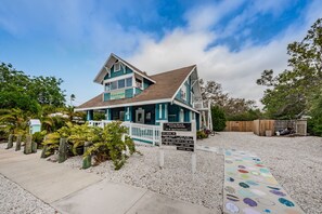 Une maison de plage à deux étages, dotée d’un porche blanc et d’une plaque indiquant les noms des principaux donateurs.