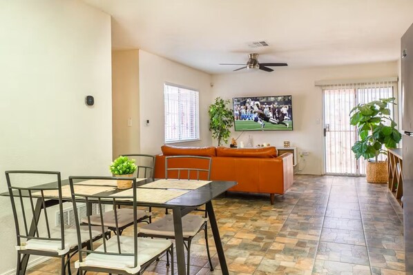 A living room with a sofa, a TV, a ceiling fan, and a dining area with chairs and a table.
