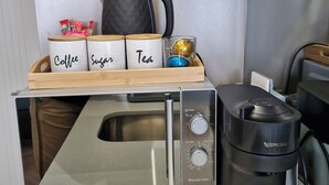 A kitchen with a coffee maker, a kettle, and labeled containers for coffee, sugar, and tea.