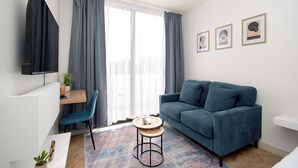 A modern living room with a blue sofa, a round coffee table, a blue chair, and a TV mounted on the wall.