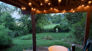 An outdoor patio with a wooden table and two chairs, surrounded by greenery and a wooden fence.