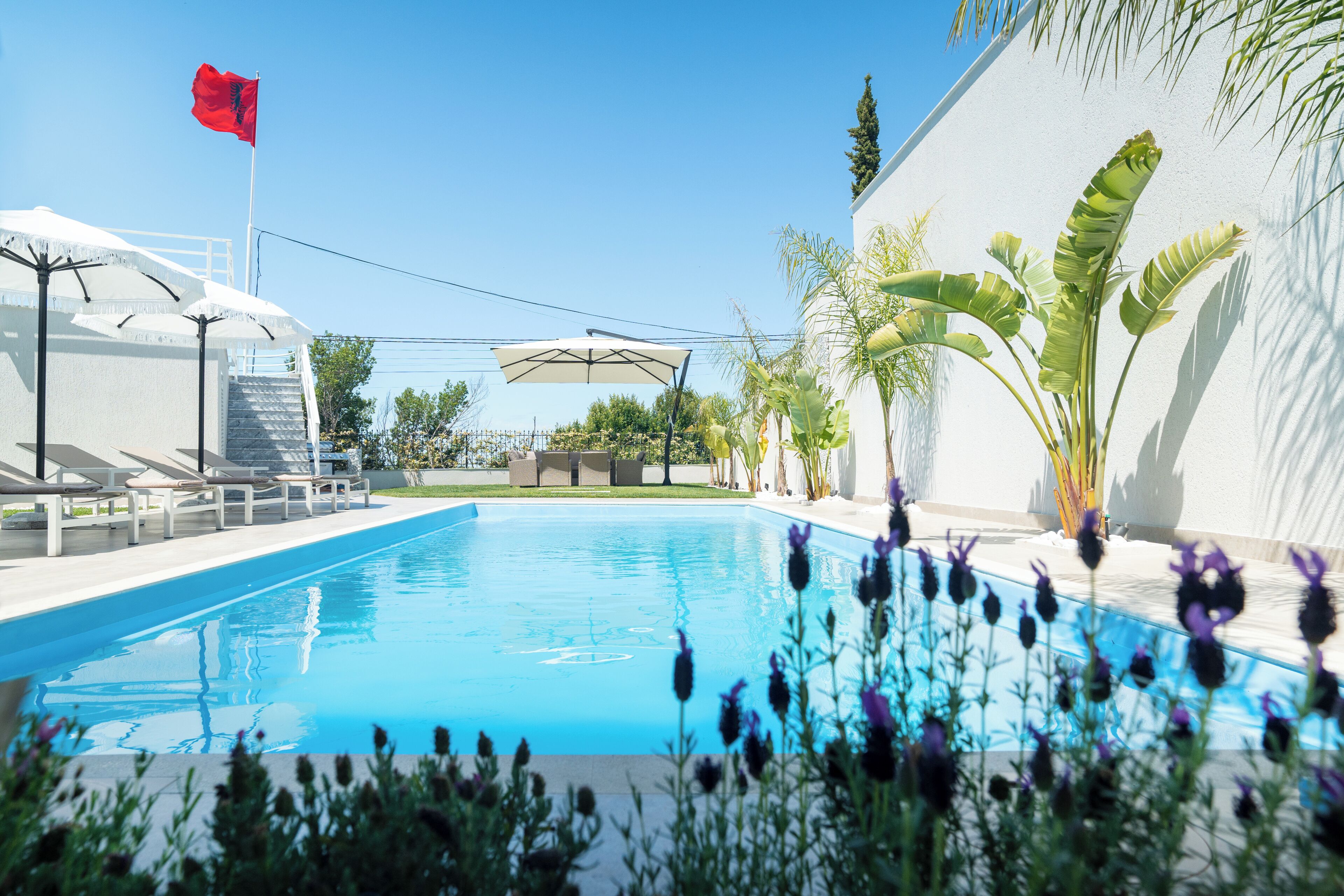 A swimming pool with a red flag, white umbrellas, and a white wall.