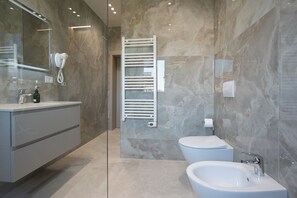 Ein modernes Badezimmer mit Marmorwand, einem weißen Waschtisch, einem Bidet und einem Handtuchhalter.