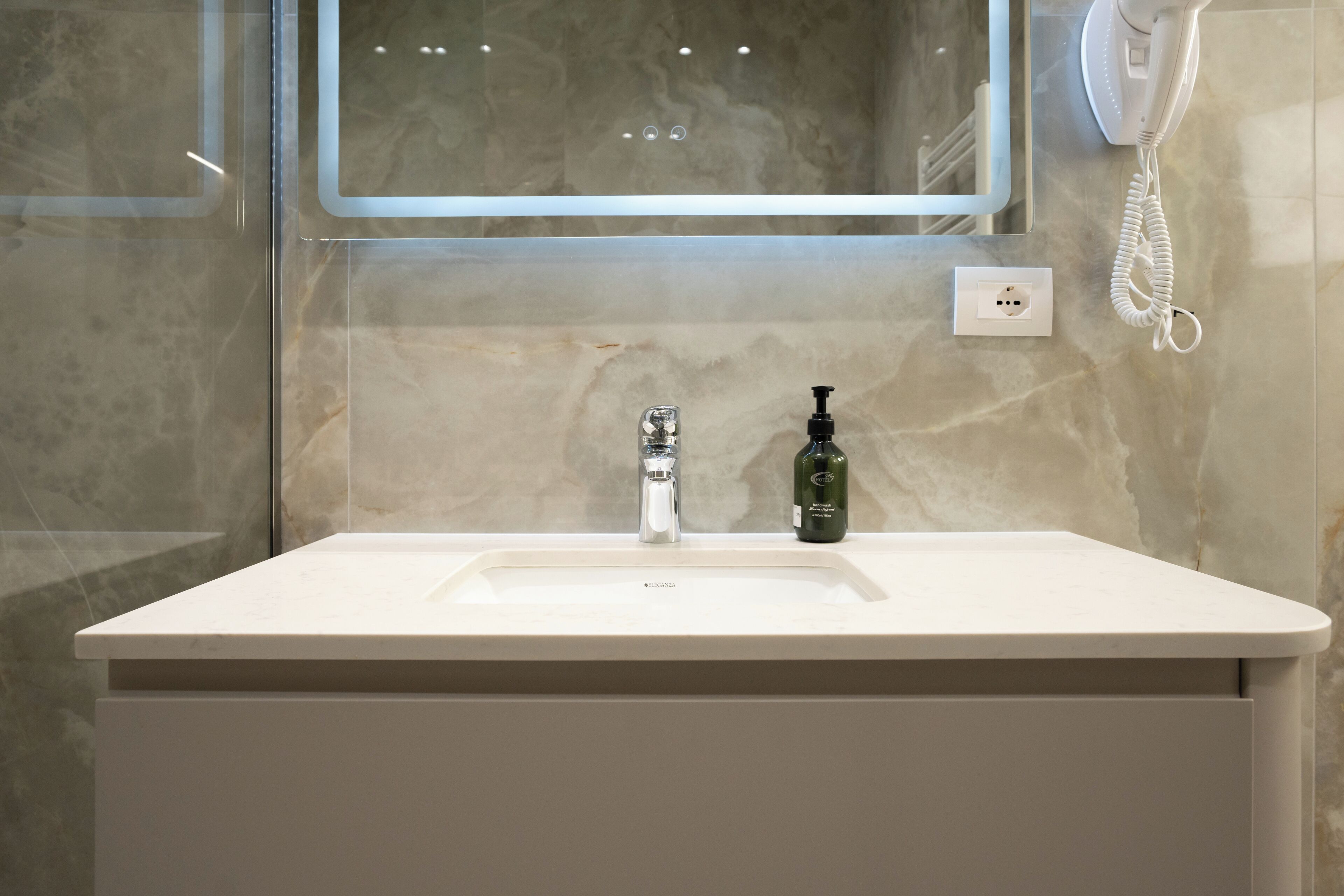 A bathroom with a white sink, a mirror, a hand dryer, and a bottle of hand soap.